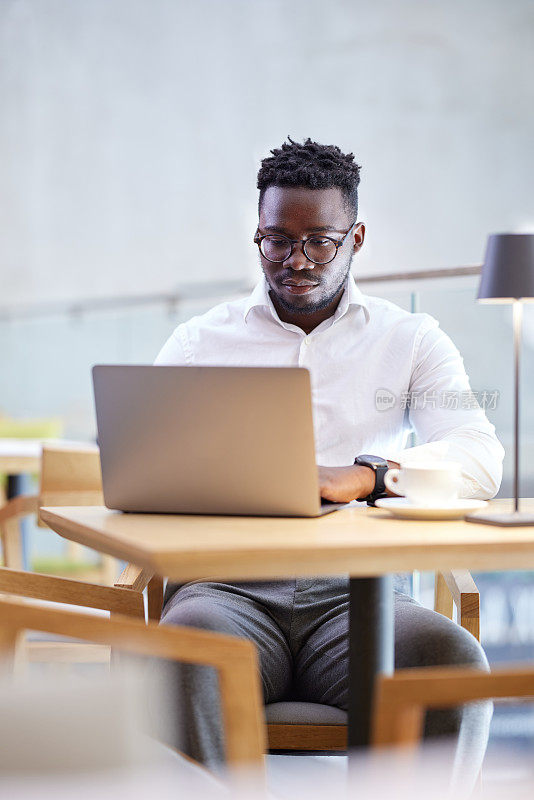 一个忙碌的非洲商人坐在自助餐厅里，在笔记本电脑上打字。
