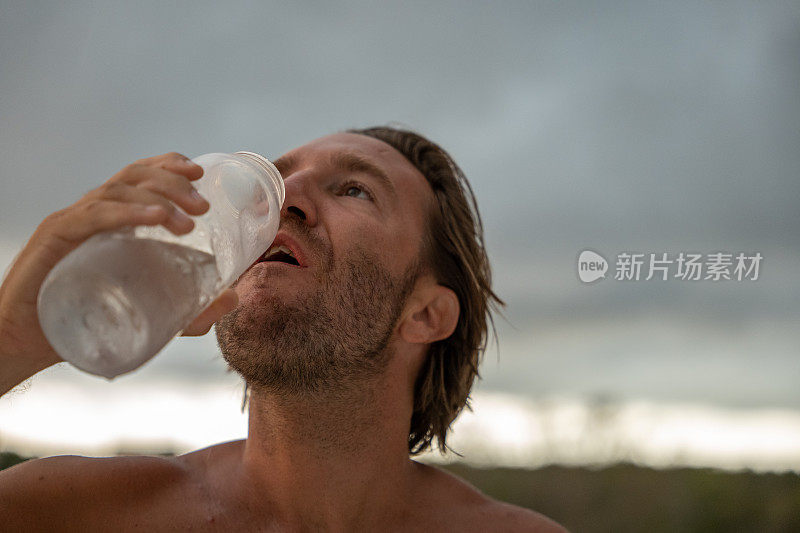 画像健康的年轻人在锻炼后喝水，他喝的是户外的水瓶