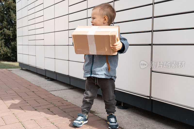 包裹投递，带储物柜的取件点，小孩拿包裹，非接触式包裹投递。儿童包裹，男孩使用自助包裹终端机发送或接收包裹
