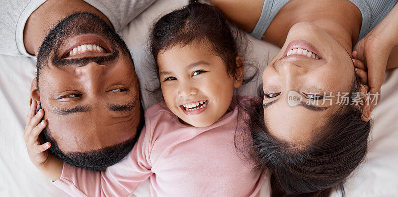 幸福的家庭与孩子躺在床上的一幅脸画像，为跨种族的爱、关怀和幸福相聚。来自墨西哥的女孩，爸爸妈妈或父母在家里放松，从上面联系