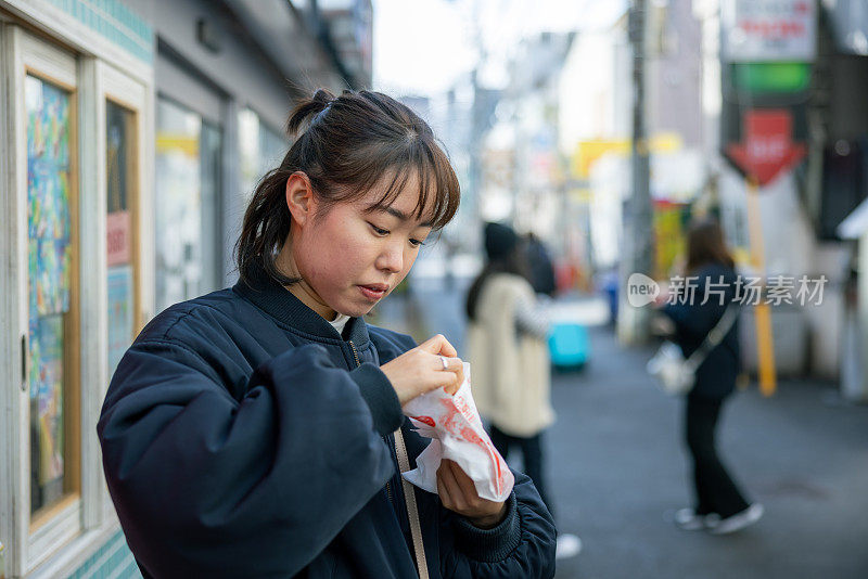 年轻女游客在街上吃韩国小吃