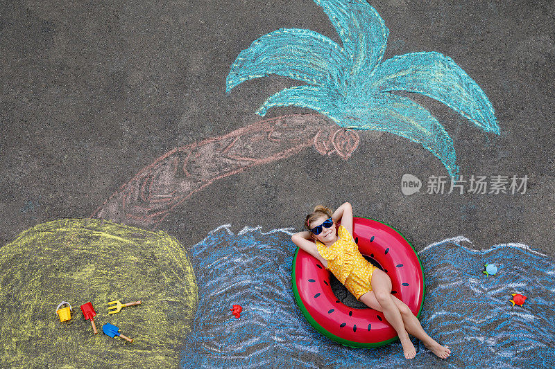 快乐的小学前班女孩在泳装充气环与海，沙子，手掌用彩色粉笔涂在沥青上。可爱的孩子与玩粉笔画的乐趣。夏天，假期，夏天