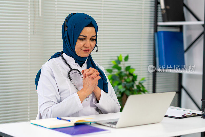 医生在线咨询病人，戴着头巾的穆斯林妇女远程用笔记本电脑进行视频通话，坐在现代化的诊所办公室里咨询病人