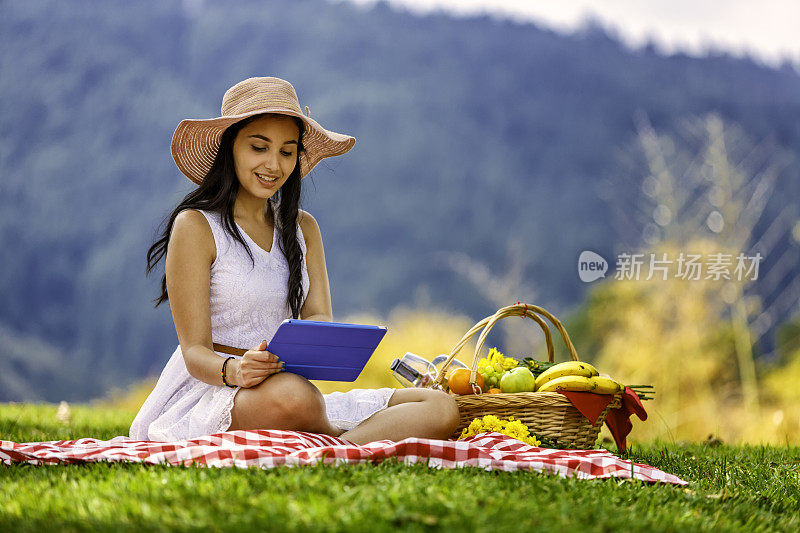 放松的年轻女子阅读平板电脑坐在草地上