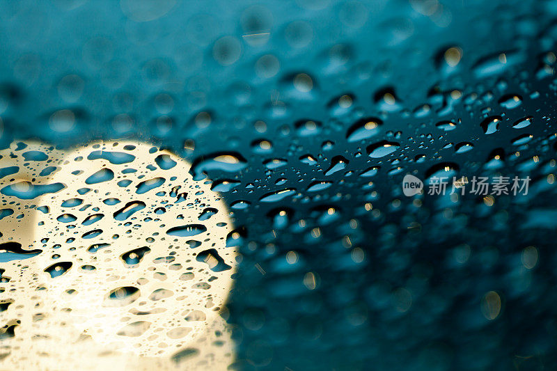 雨点落在挡风玻璃上，车头灯在背景中