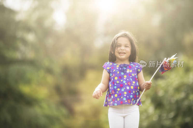 小女孩拿着风车在夏天的田野里