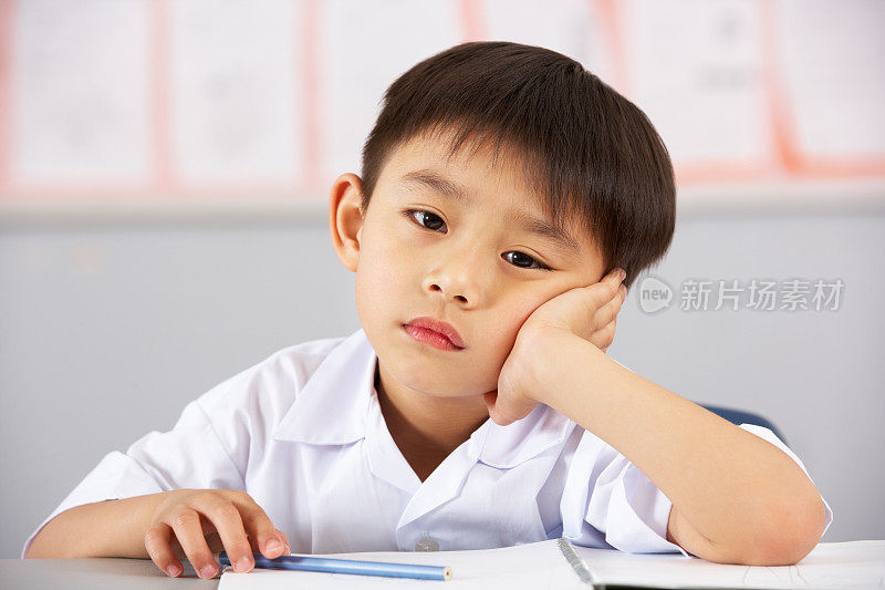 在中国学校的课桌上工作的不快乐的男学生