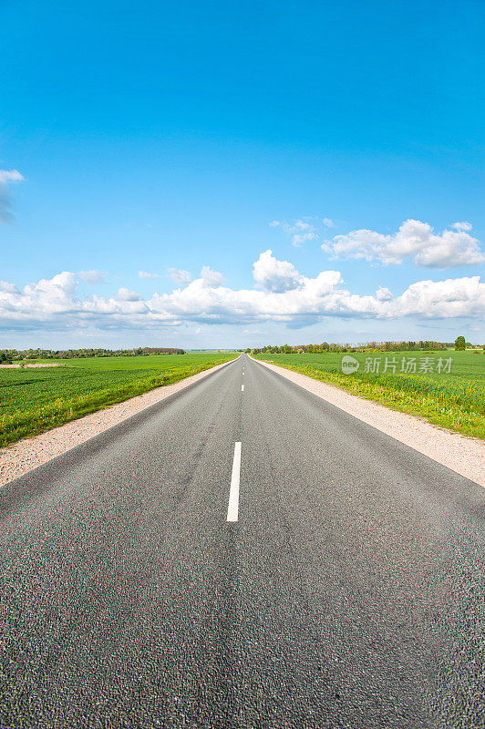 柏油路在绿色的田野上，在蓝色多云的天空背景下