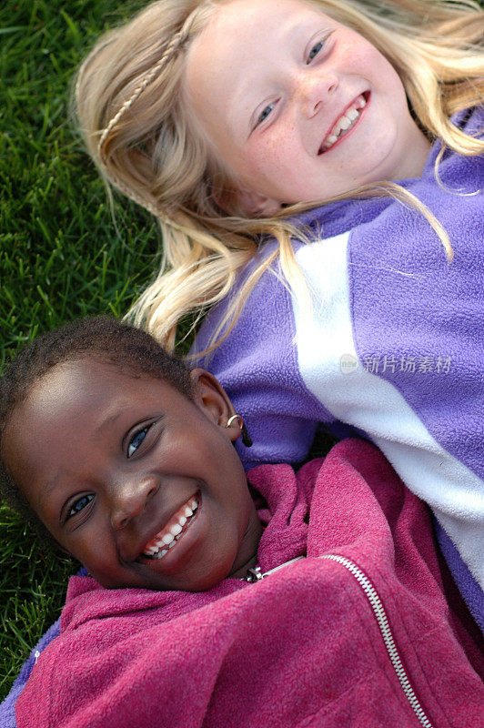 两个快乐的女孩微笑着躺在草地上
