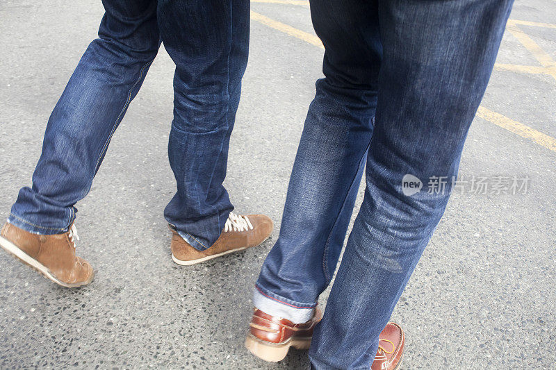 两个年轻人穿着牛仔裤走在柏油路上。