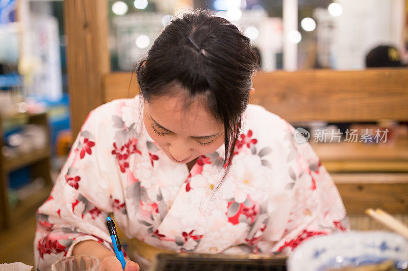 年轻的浴方女子在日本居酒屋餐厅写东西