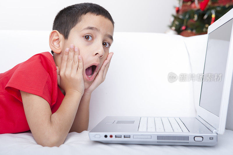 圣诞节震惊的男孩在用笔记本电脑
