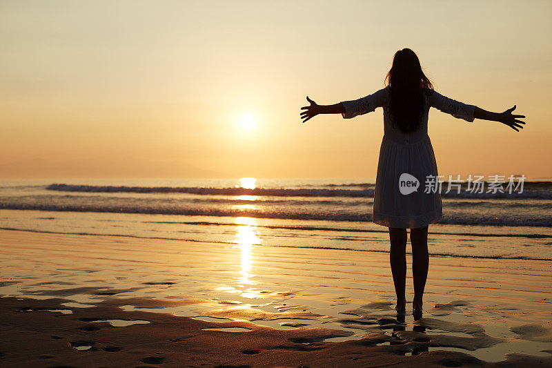 全身的女人在阳光下在海滩上伸开双臂