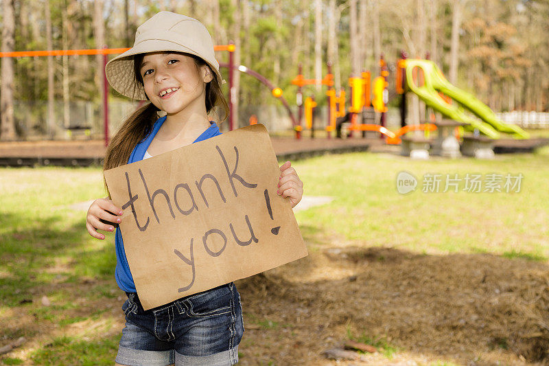 志愿者服务:可爱的小女孩拿着“谢谢”的牌子。当地的公园。