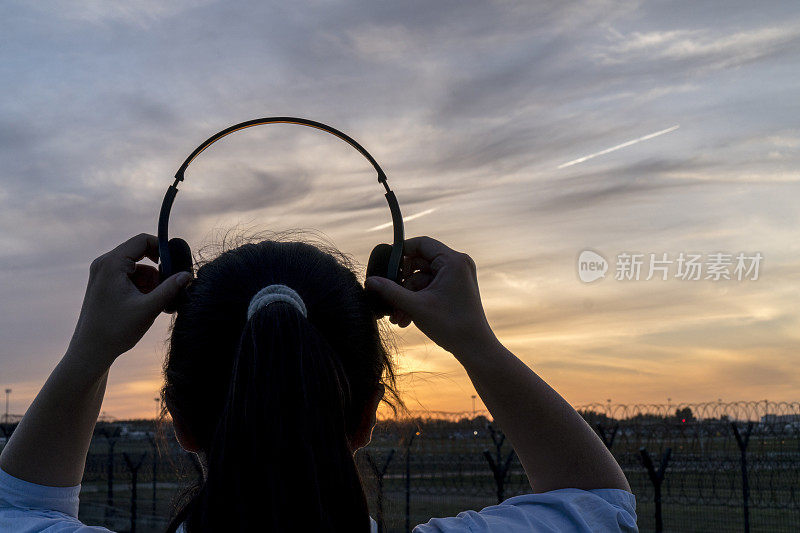 女孩戴着耳机，面对夕阳