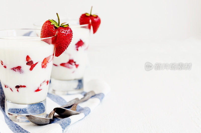 甜点酸奶和草莓层在一个玻璃上的蓝色条纹餐巾在白色的背景