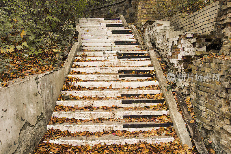 废弃的楼梯被漆成钢琴键的风格，周围是秋天飘落的黄叶和倒塌的墙壁。概念上，象征着秋天悲伤的音乐、歌曲或交响乐
