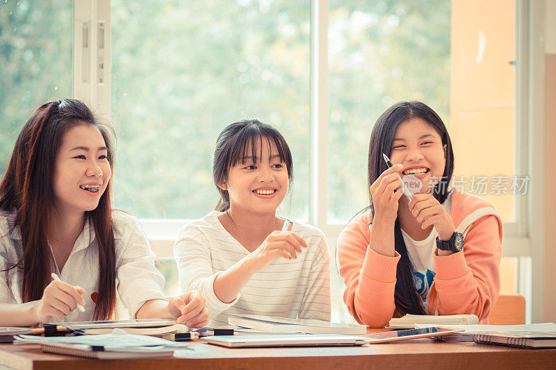 快乐的亚洲年轻女子在做小组学习。亚洲大学或大学生在教室的窗边与平板电脑、笔记本电脑和报告文件一起学习。教育类的概念