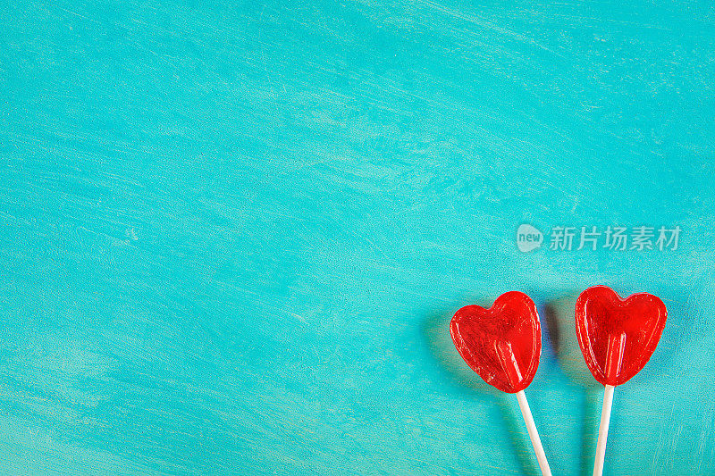 两个红心形状的糖果棒棒糖在绿松石背景角落的位置。情人节浪漫爱情贺卡横幅海报拷贝空间。创意优雅简约风格