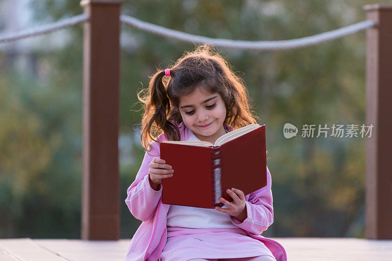 快乐的女孩坐在公园里看书。