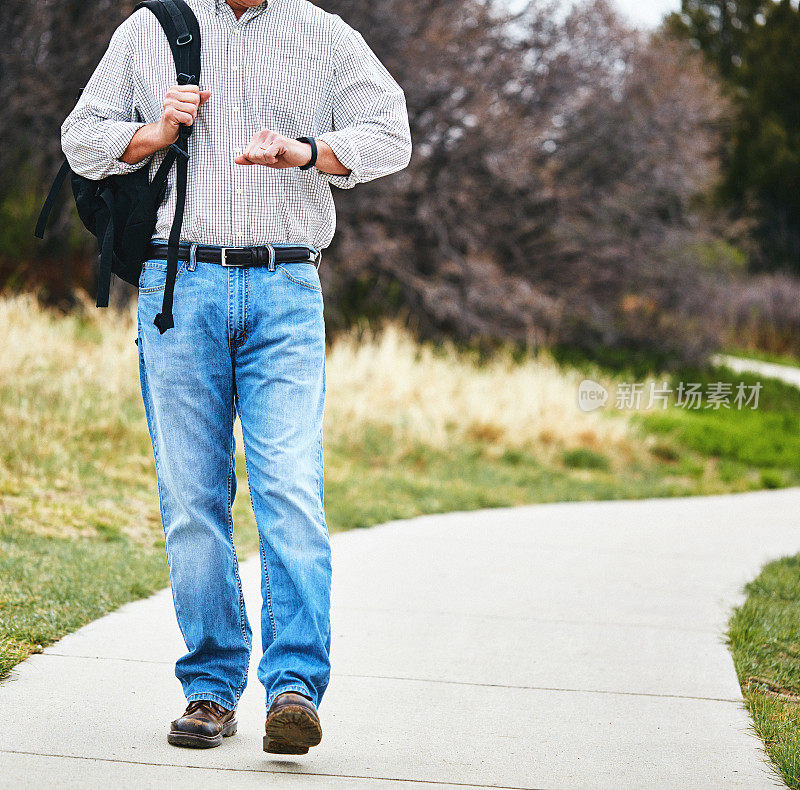 成年男性穿着休闲服装走路检查健身追踪器上的数据