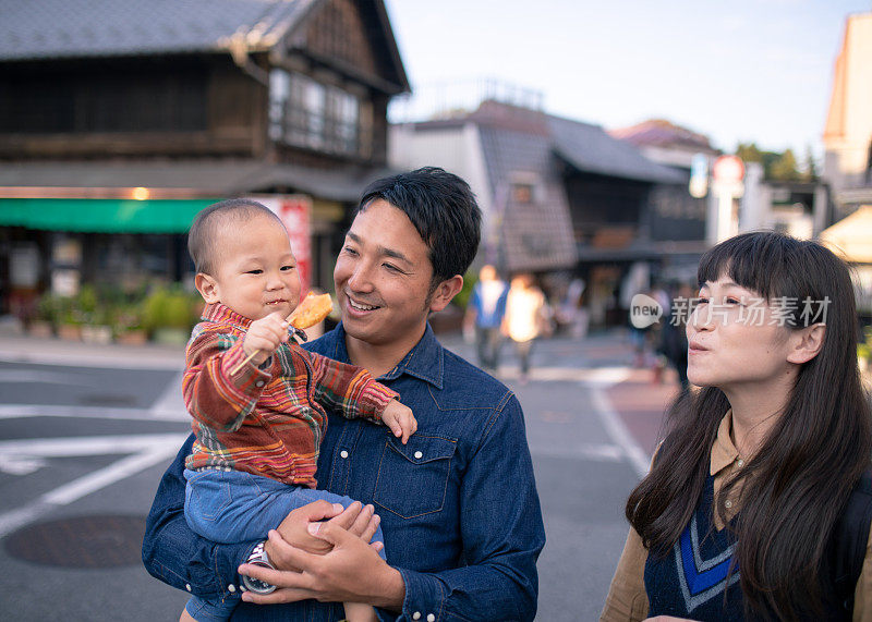 年轻的家庭在传统的日本街道上吃“Senbei”日本米饼