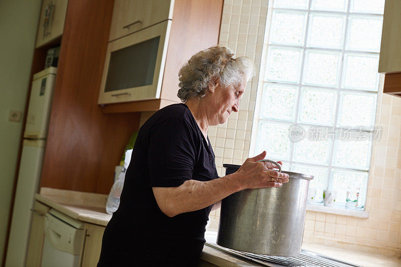 一位老妇人在厨房里拿着一个巨大的锅子准备食物