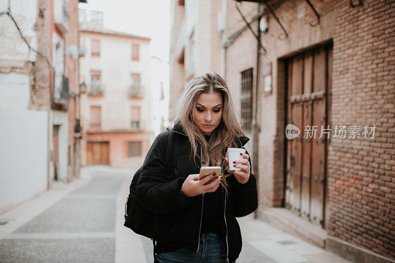 年轻女子拿着外带咖啡杯看着智能手机