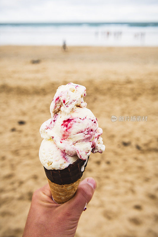 在Fistral海滩，纽基，康沃尔，手持一个大覆盆子涟漪冰淇淋。