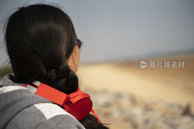 年轻女性戴着耳机躺在沙滩上