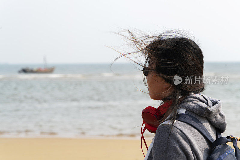 年轻女性戴着耳机躺在沙滩上