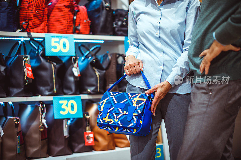 一位老年妇女和她的伴侣在一家手提包和饰品店试用一个蓝色的小手提包