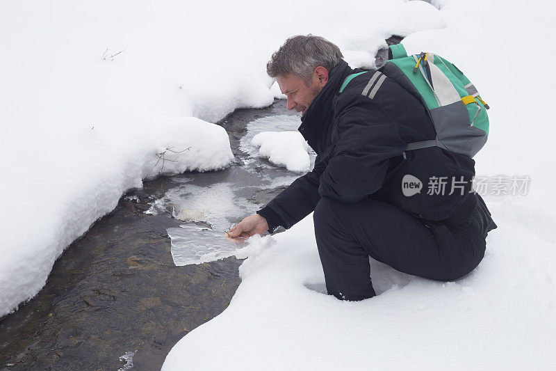 快乐的成年人徒步旅行在下雪的冬天的自然。清凉的冰冻森林溪流。