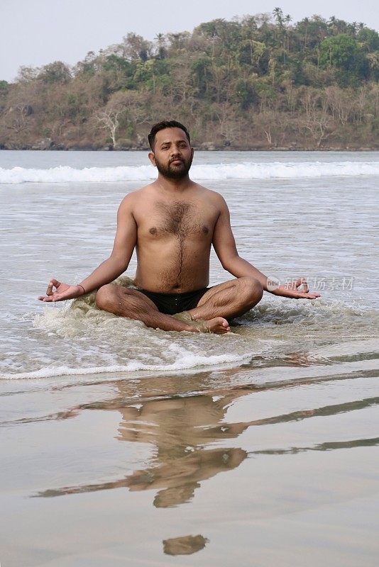 赤裸胸部的印度男子练习莲花姿势(莲花瑜伽)瑜伽位置在潮湿的沙滩上，水的边缘，帕洛伦海滩，果阿，印度