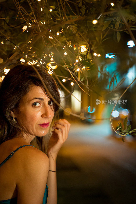 在巴塞罗那的街道上，一个优雅的女人在装饰灯光下