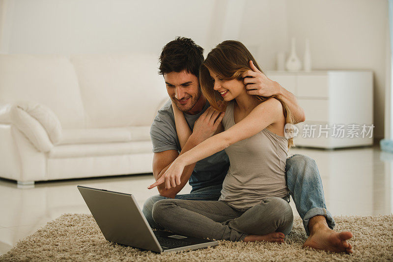 年轻女子指着笔记本电脑屏幕，而她和她的男朋友正在使用它