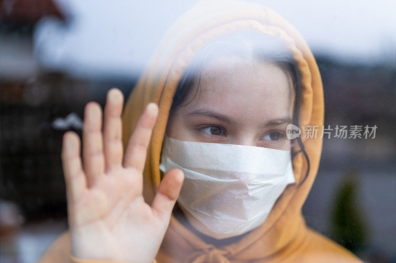 一个戴着外科口罩的少女站在窗前看