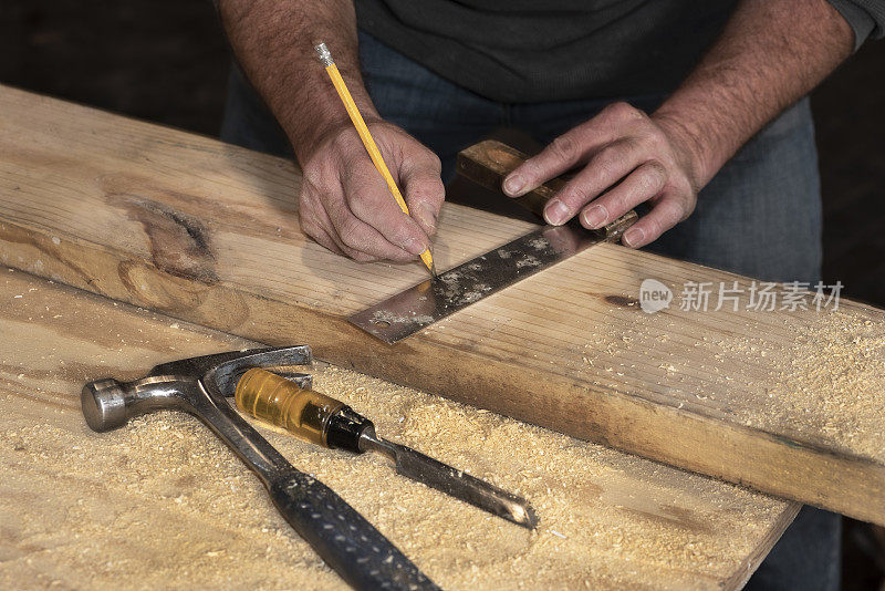 在建筑工地上，一名男木匠在木板上画了一条线，以便切割