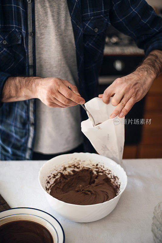 检疫烹饪:检疫烹饪:一名男子正在将巧克力奶油放入糖衣袋，以填满甜点
