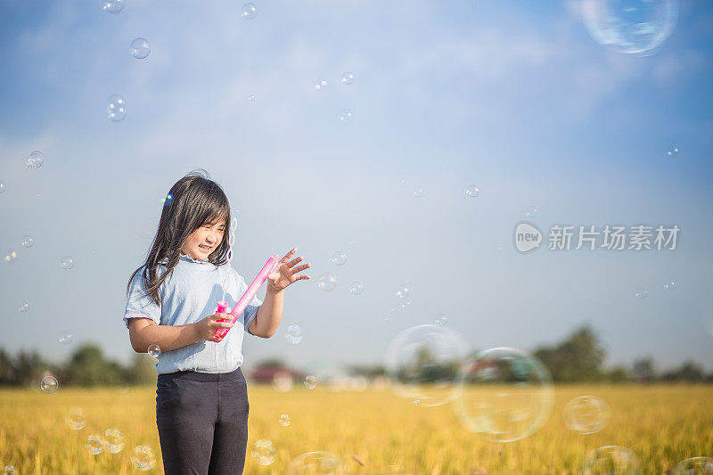 一个可爱的亚洲中国女孩玩肥皂泡在稻田在阳光灿烂的周末。