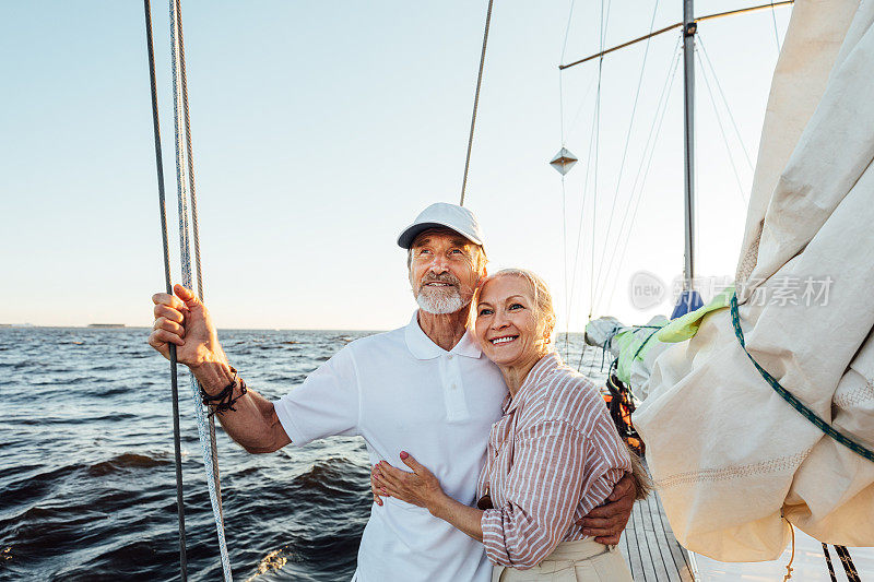 相爱的老年夫妇享受假期，遥望远方。一对成熟的情侣站在一起，拥抱在一艘私人帆船上。