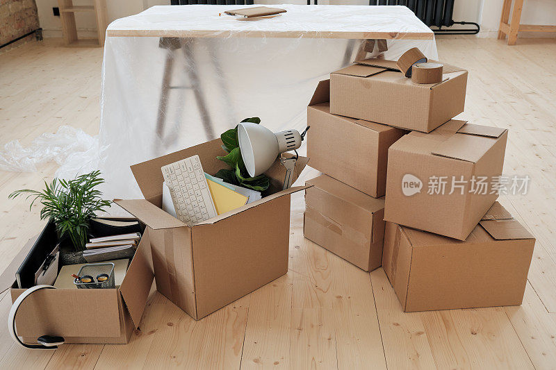 在新办公室里，移动办公物品的盒子堆叠在地板上，书桌上覆盖着聚乙烯