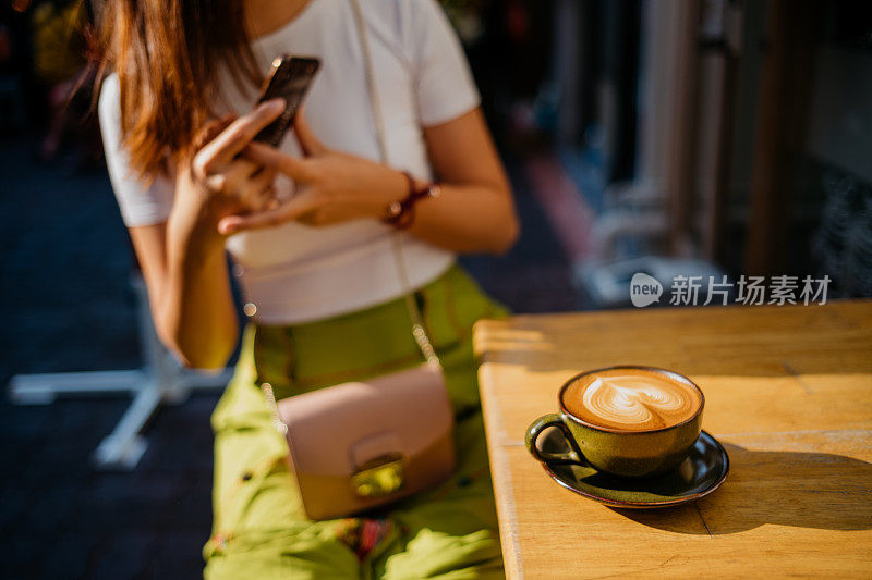 年轻的亚洲女人用智能手机拍她的拿铁咖啡