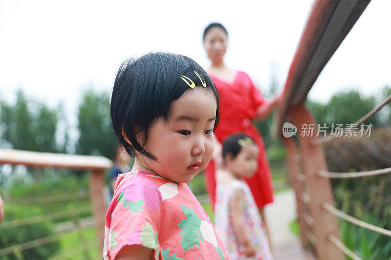 一个中国女孩看着公园里的小路，她的姐姐和妈妈在后面