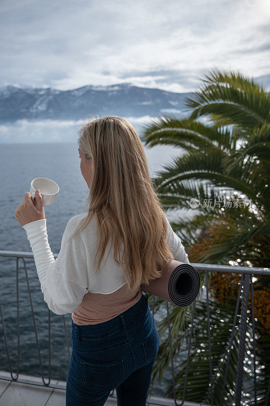 年轻女子在她的阳台上享受湖景，一杯茶在早上