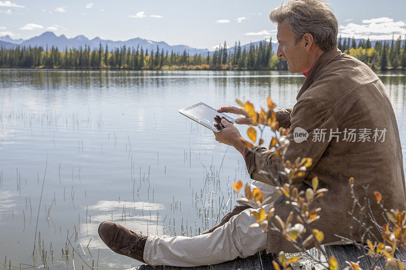 早晨在高山湖边用平板休息的男人