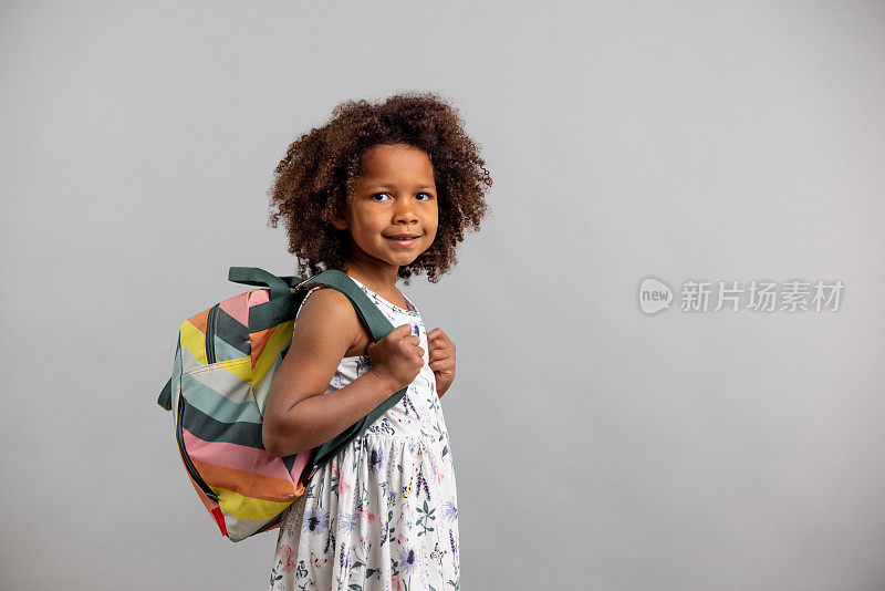 一个年幼的学前班女孩拿着书包的侧面照片