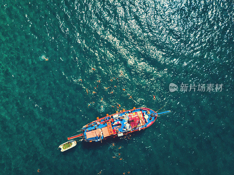 红色游船在炎热夏日的鸟瞰图。俯视图的人正在船周围游泳