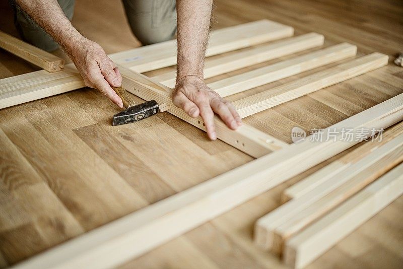一个男人的手拿着锤子试图组装床的特写