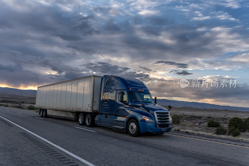一辆大型商业货运半挂车在沙漠公路上向东行驶，以交付货物，一个戏剧性的日落背景